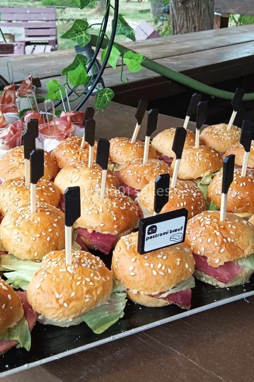 Plateau de mini-burgers au pastrami de bœuf avec salade, présentés sur une table en bois en extérieur.