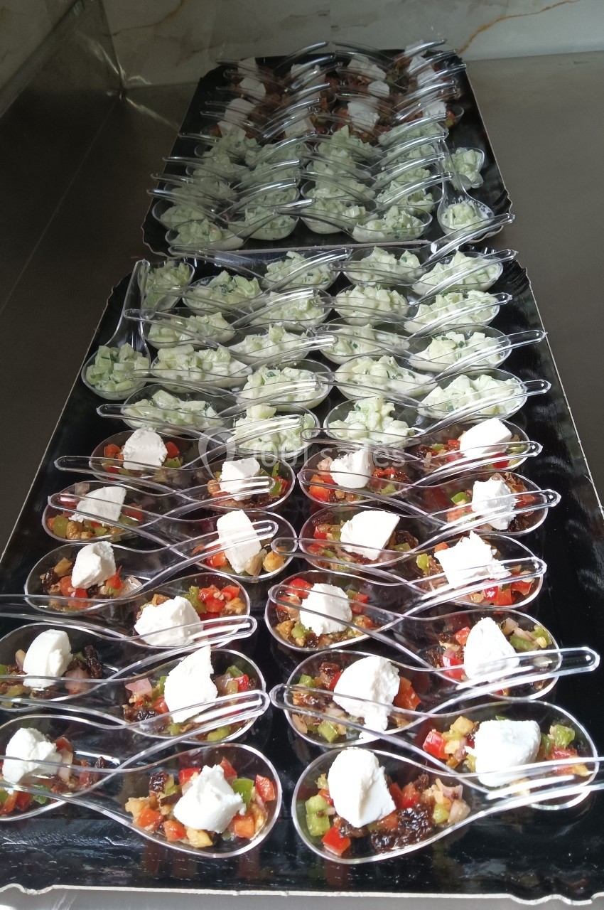 Cuillères apéritives garnies de légumes colorés, fromage frais et salade de concombre, disposées sur un plateau noir.