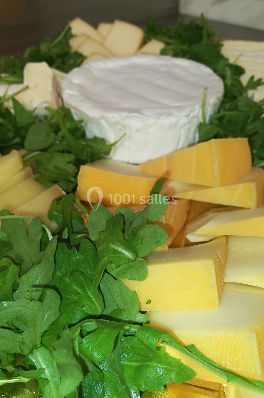 Plateau de fromages variés entouré de feuilles de roquette, avec un fromage à pâte molle au centre.