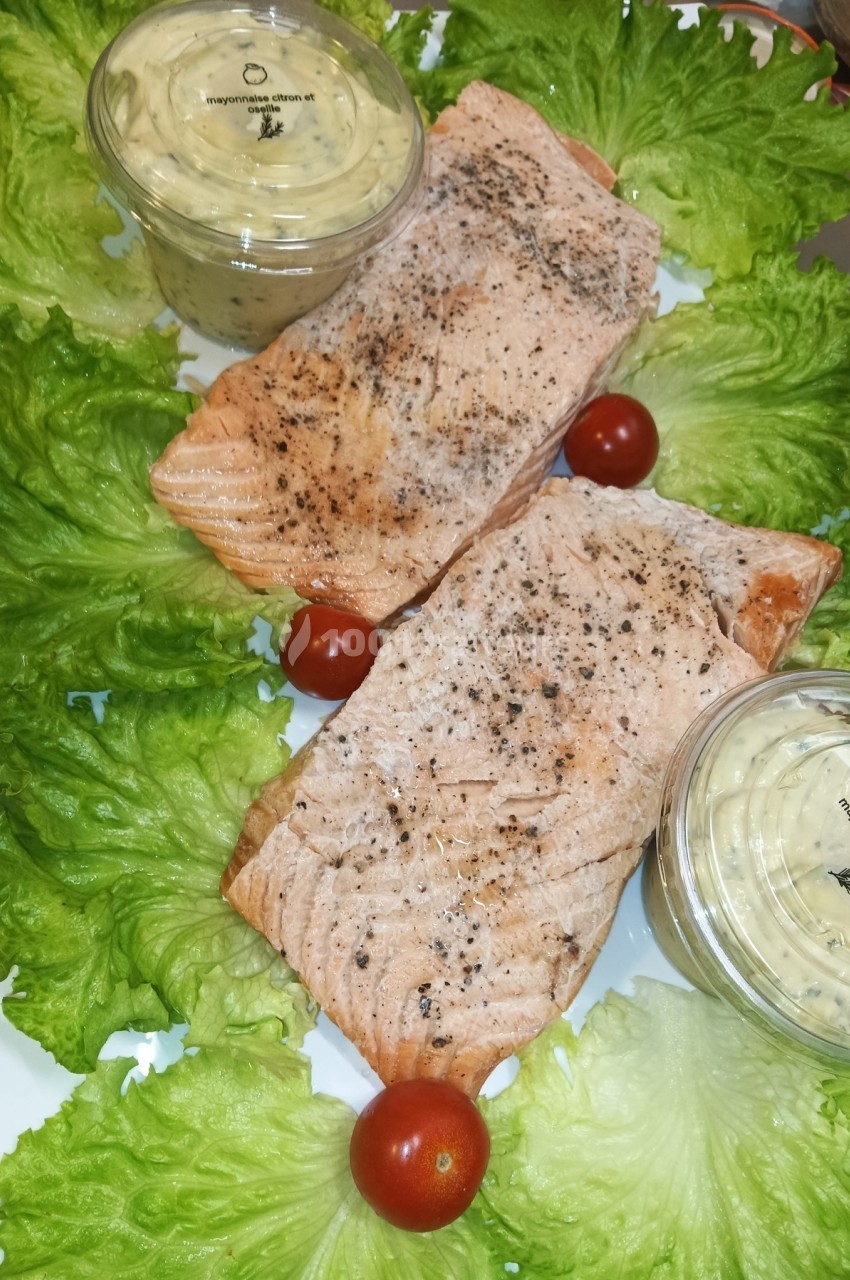 Deux pavés de saumon grillés sur un lit de feuilles de salade, accompagnés de tomates cerises et de sauce en pot.