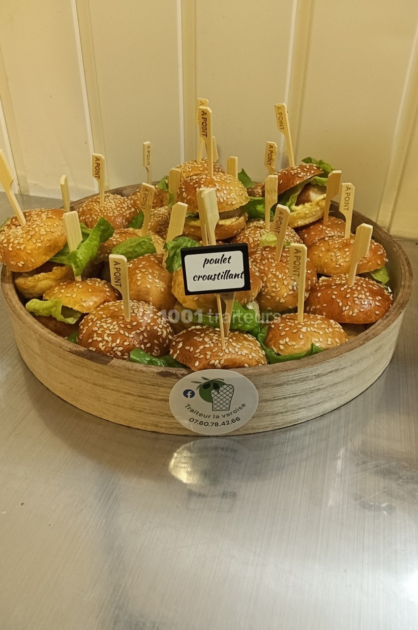 Plateau de mini-burgers au poulet croustillant avec salade, servis avec des piques en bois, sur une table en inox.