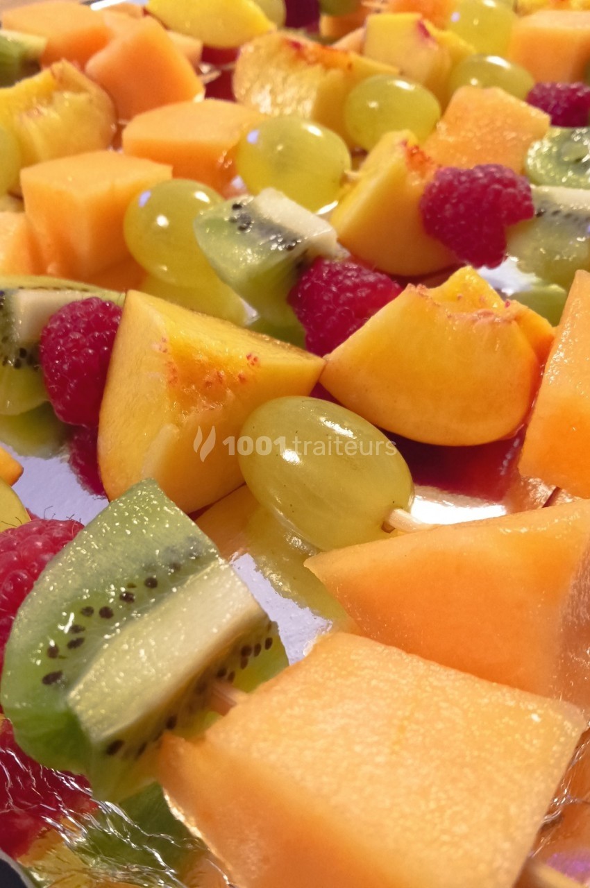 Assortiment de brochettes de fruits frais avec melon, kiwi, raisin, pêche et framboise sur un plateau.