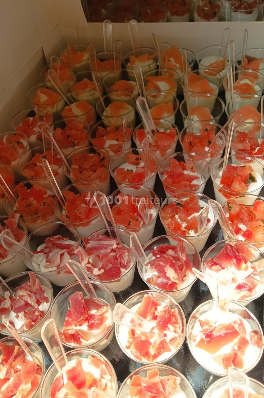 Verrines variées contenant des morceaux de jambon, saumon et melon, présentées sur un plateau avec des cuillères.