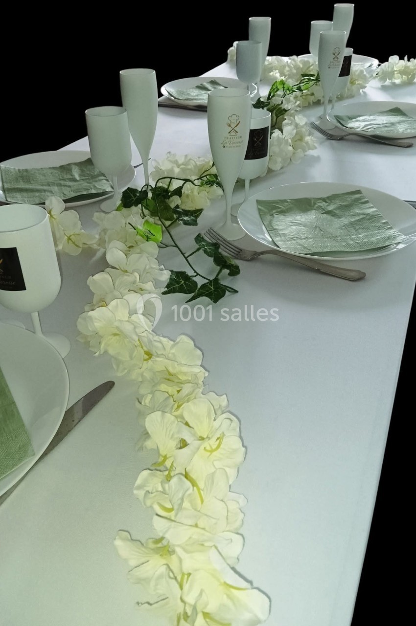 Table dressée avec une nappe blanche, serviettes vertes, vaisselle blanche et décoration florale blanche et verte.