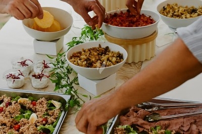 Buffet avec plateau de charcuterie, pommes de terre, salades variées et décoration florale dans une salle de réception.