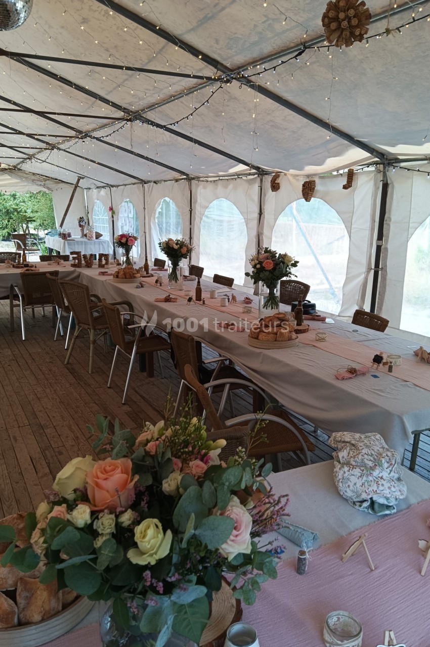 Salle de réception sous chapiteau avec tables décorées de nappes, bouquets de fleurs et guirlandes lumineuses.