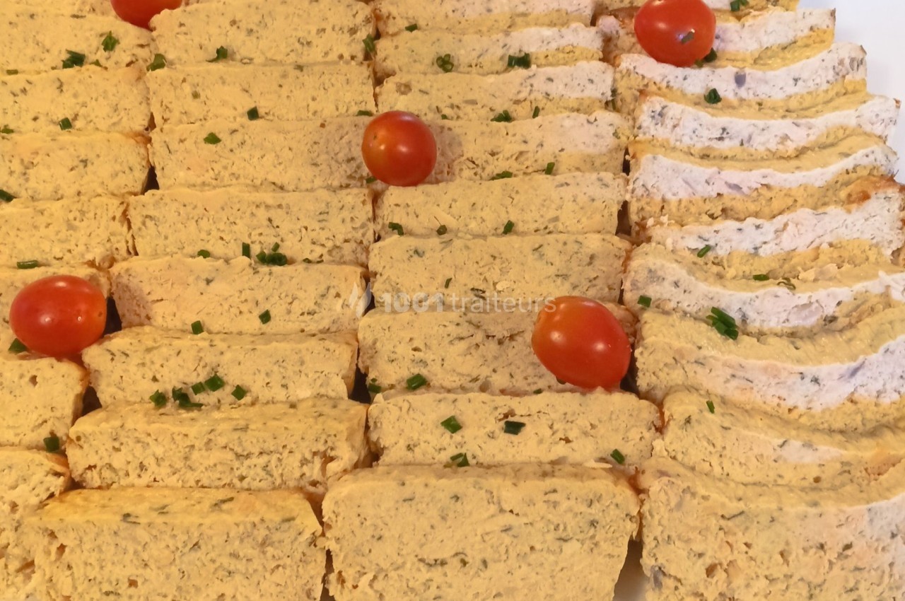 Plateau de tranches de terrine garnies de ciboulette et de tomates cerises, présenté sur un fond de feuilles vertes.