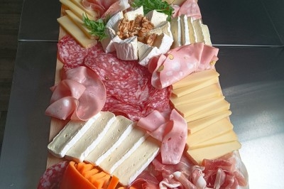 Buffet avec plateau de charcuterie, pommes de terre, salades variées et décoration florale dans une salle de réception.