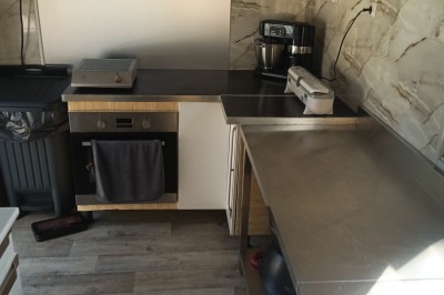 Plan de travail en acier inoxydable sous une fenêtre à double vitrage, dans une pièce aux murs carrelés effet marbre.