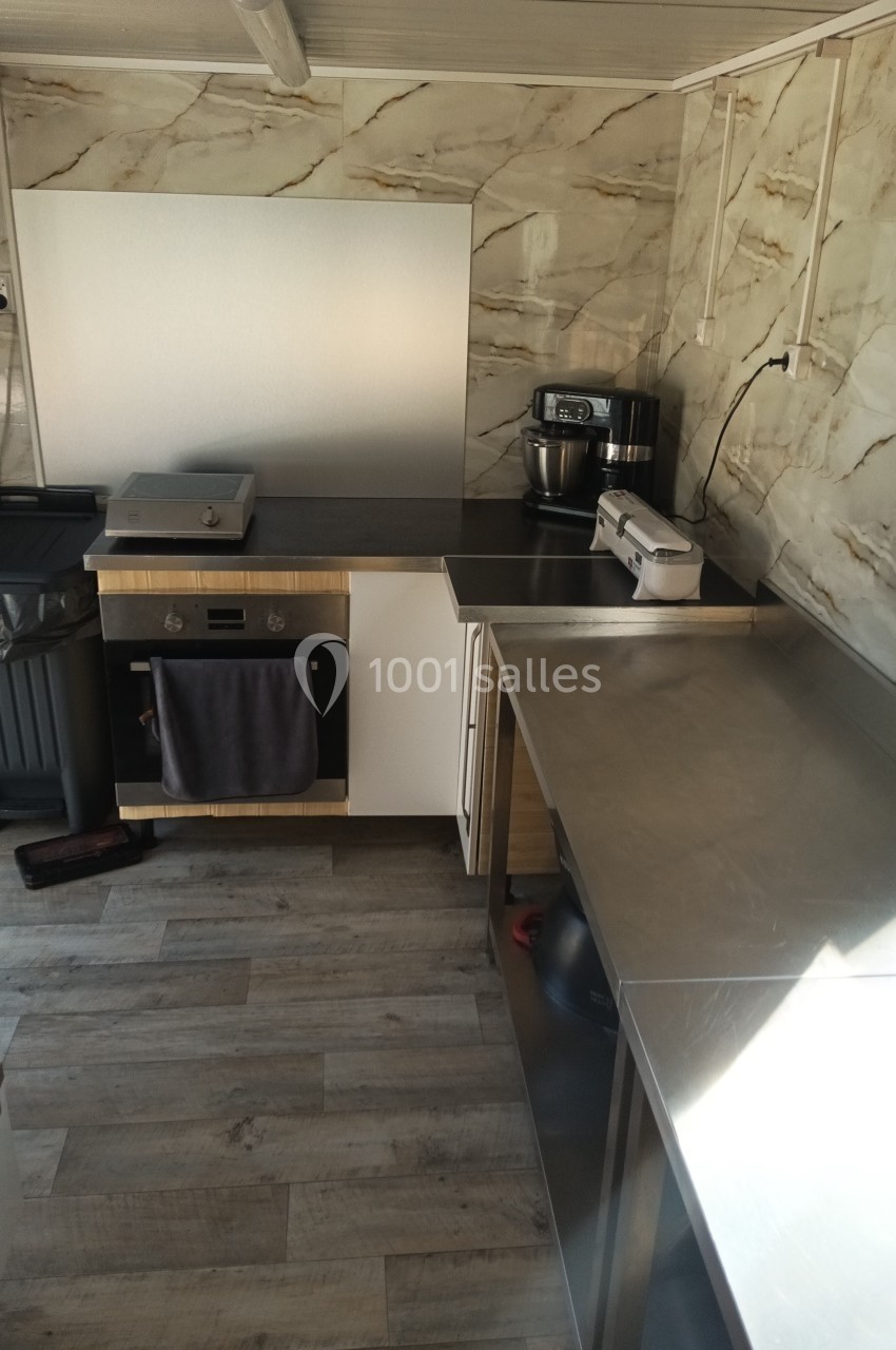 Cuisine équipée avec plan de travail en inox, four encastré, robot de cuisine et murs au revêtement effet marbre.