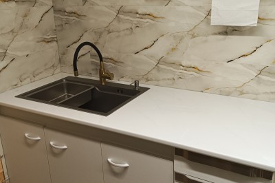 Plan de travail en acier inoxydable sous une fenêtre à double vitrage, dans une pièce aux murs carrelés effet marbre.