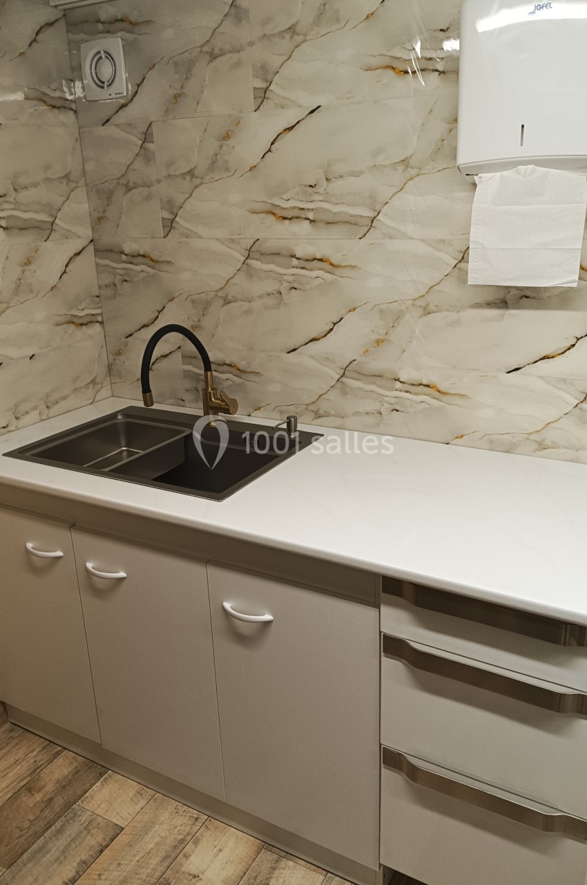 Évier double avec robinet noir et plan de travail blanc dans une cuisine aux murs effet marbre et sol en bois.