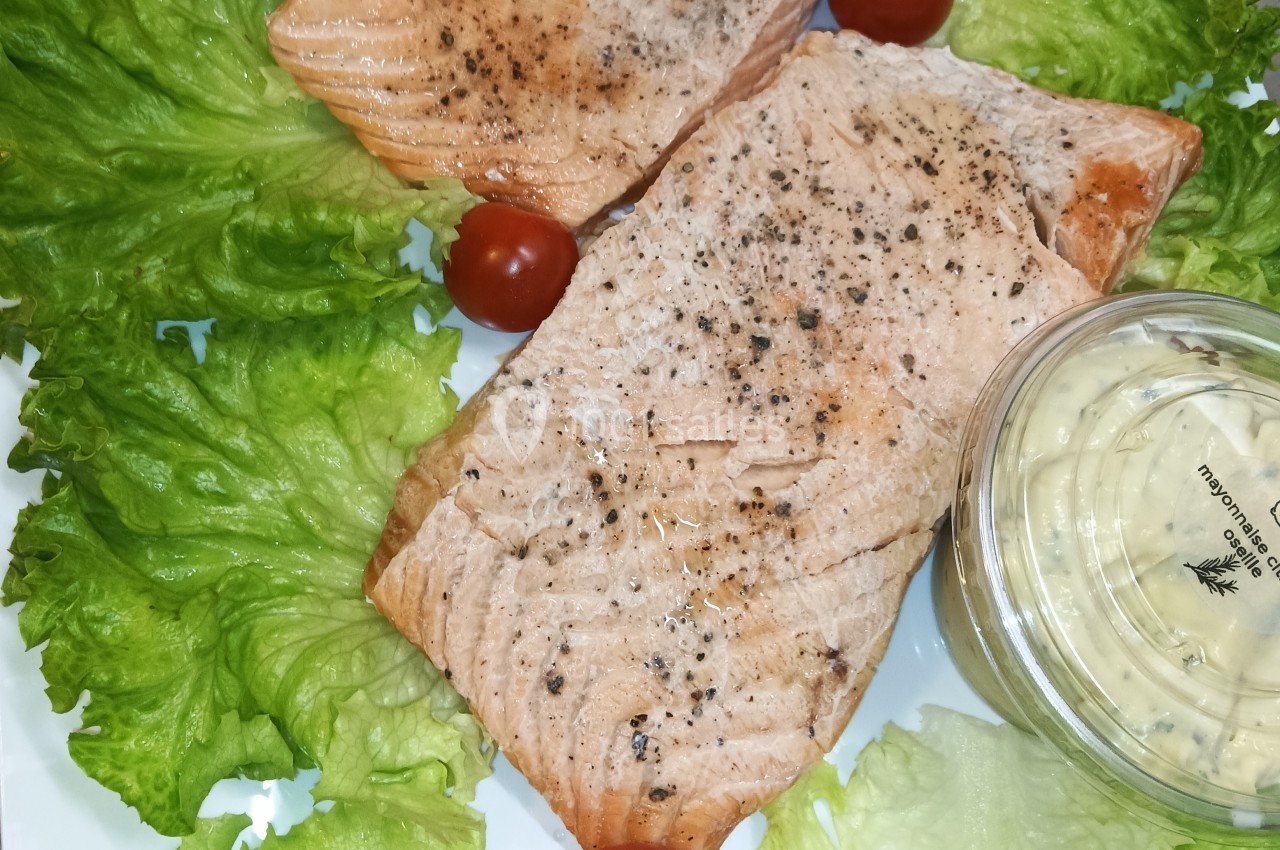 Filets de saumon grillés assaisonnés, accompagnés de feuilles de laitue, tomates cerises et sauce en pot.