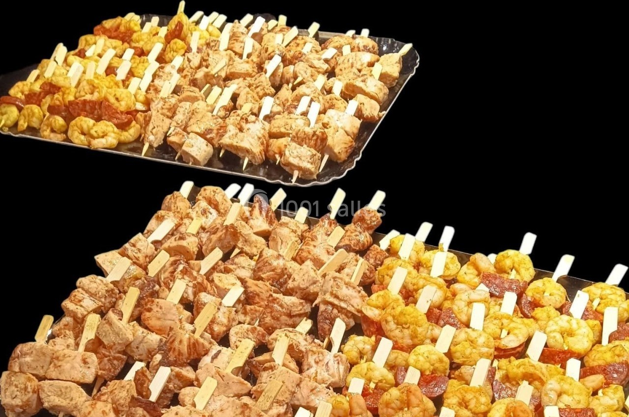 Plateaux de brochettes variées comprenant viandes marinées, crevettes et morceaux de fromage sur fond noir.