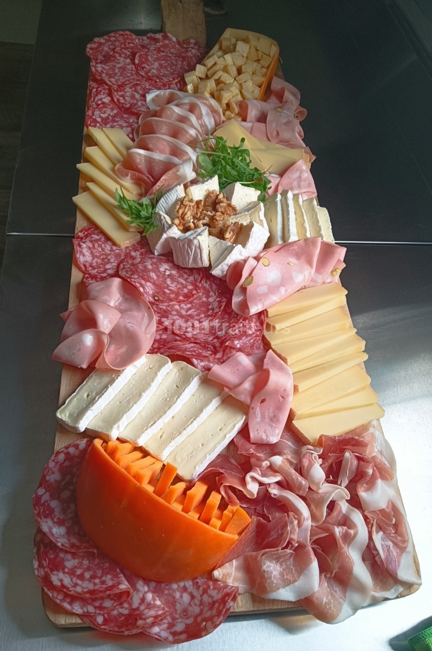 Plateau de charcuteries et fromages variés disposés sur une planche en bois, accompagné de noix et de roquette.