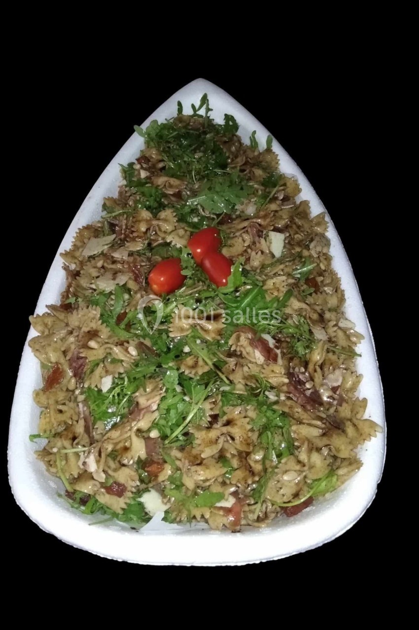 Plat de pâtes en forme de nœuds papillon, garni de roquette, tomates cerises et morceaux de viande.