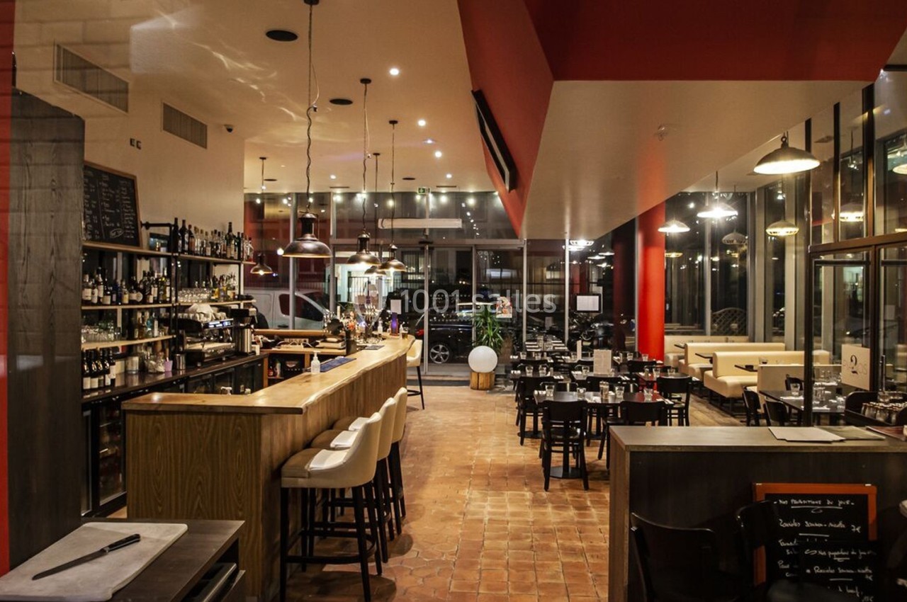 Intérieur d'un restaurant moderne avec bar en bois, tables dressées et éclairage chaleureux.
