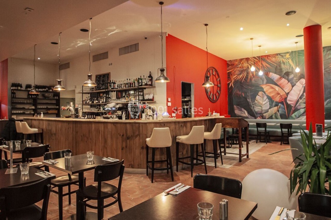 Salle de restaurant moderne avec un bar en bois, des tables dressées et une fresque murale colorée en arrière-plan.