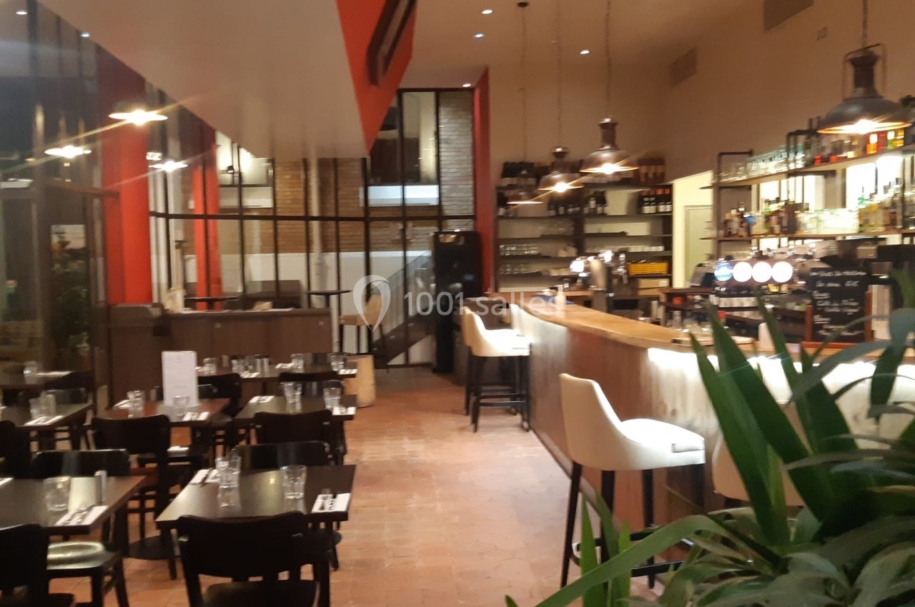 Intérieur d'un restaurant moderne avec tables dressées, bar éclairé et décoration végétale.