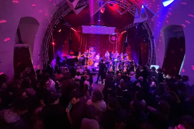Façade d'un café-restaurant avec terrasse extérieure, tables et chaises sous un auvent rouge marqué ’Les 2 Pianos’.