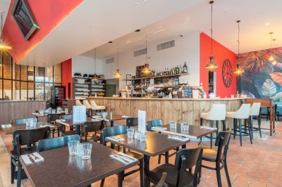 Façade d'un café-restaurant avec terrasse extérieure, tables et chaises sous un auvent rouge marqué ’Les 2 Pianos’.