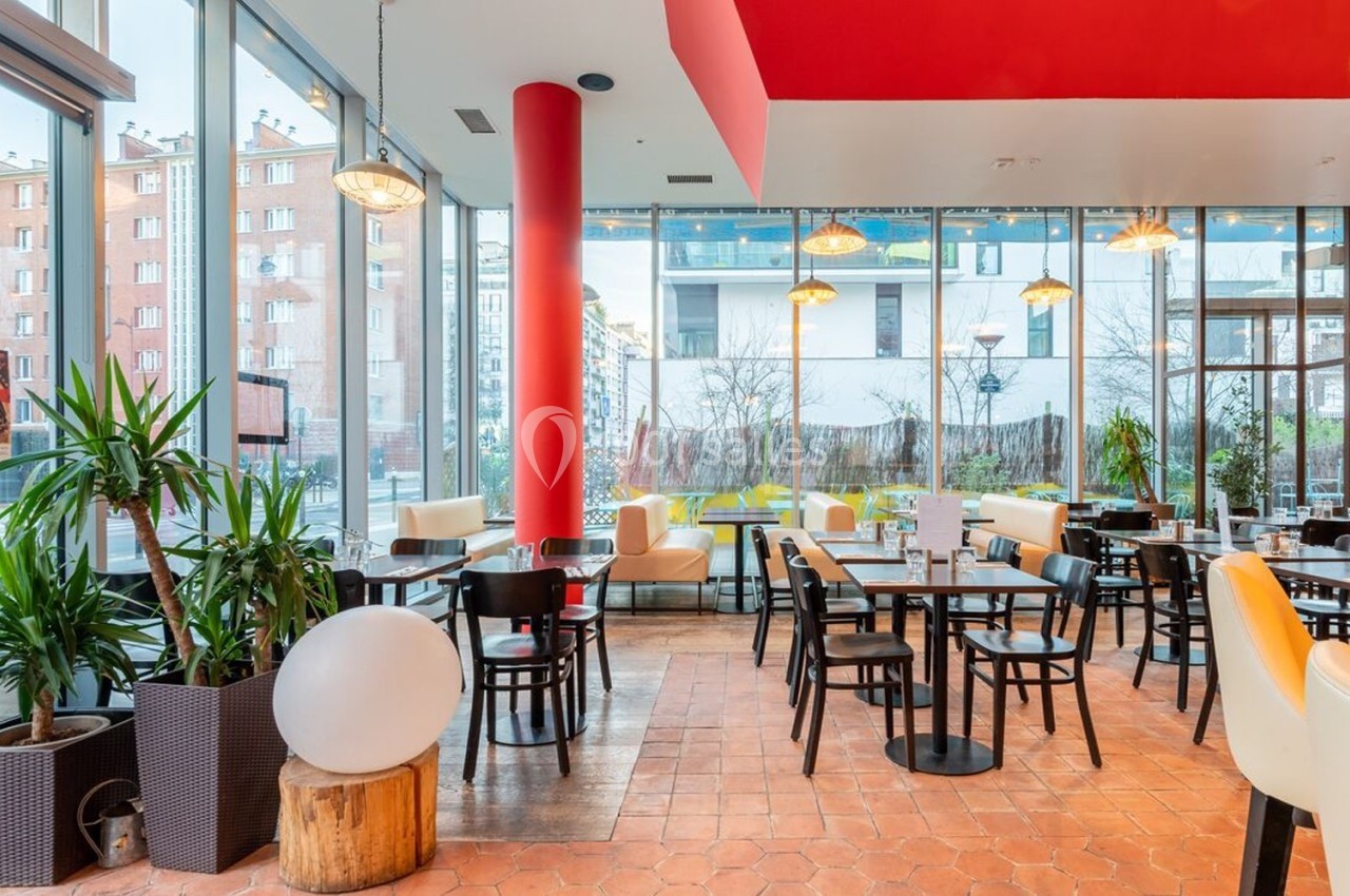 Salle de restaurant lumineuse avec grandes baies vitrées, mobilier moderne et plantes décoratives.