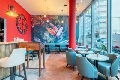 Façade d'un café-restaurant avec terrasse extérieure, tables et chaises sous un auvent rouge marqué ’Les 2 Pianos’.