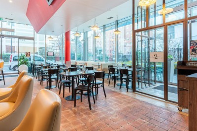 Façade d'un café-restaurant avec terrasse extérieure, tables et chaises sous un auvent rouge marqué ’Les 2 Pianos’.