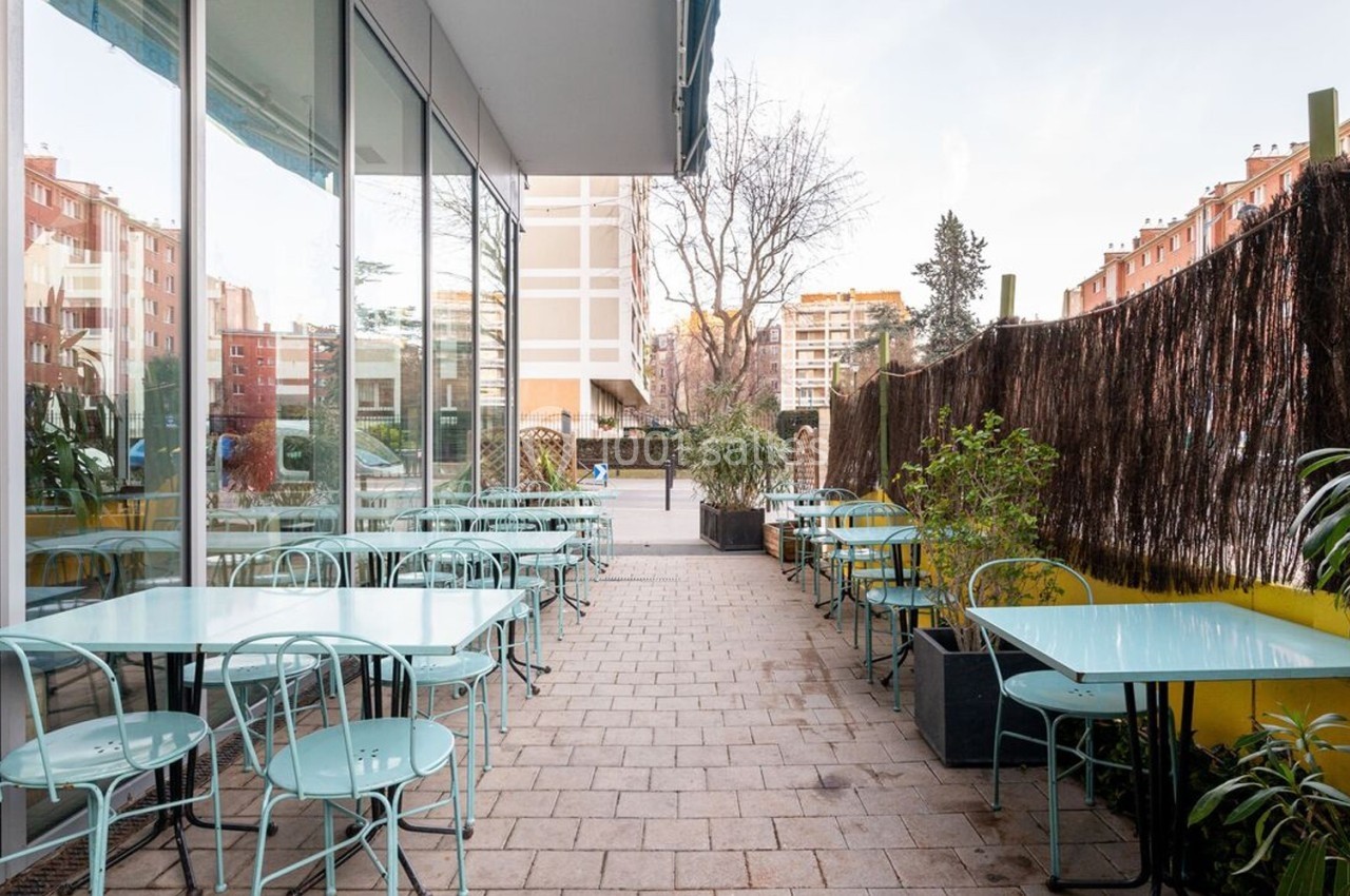 Terrasse extérieure avec tables et chaises en métal bleu clair, entourée de plantes et bordée d'une clôture en bois.