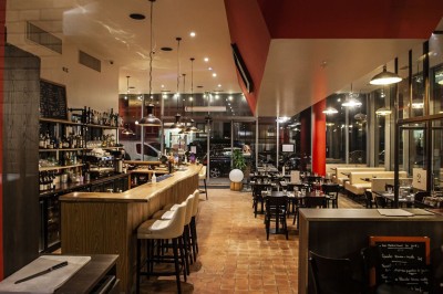 Façade d'un café-restaurant avec terrasse extérieure, tables et chaises sous un auvent rouge marqué ’Les 2 Pianos’.