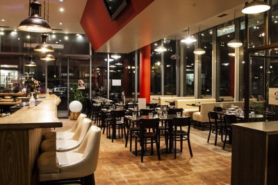 Façade d'un café-restaurant avec terrasse extérieure, tables et chaises sous un auvent rouge marqué ’Les 2 Pianos’.