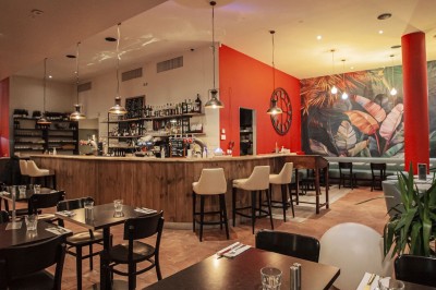 Façade d'un café-restaurant avec terrasse extérieure, tables et chaises sous un auvent rouge marqué ’Les 2 Pianos’.