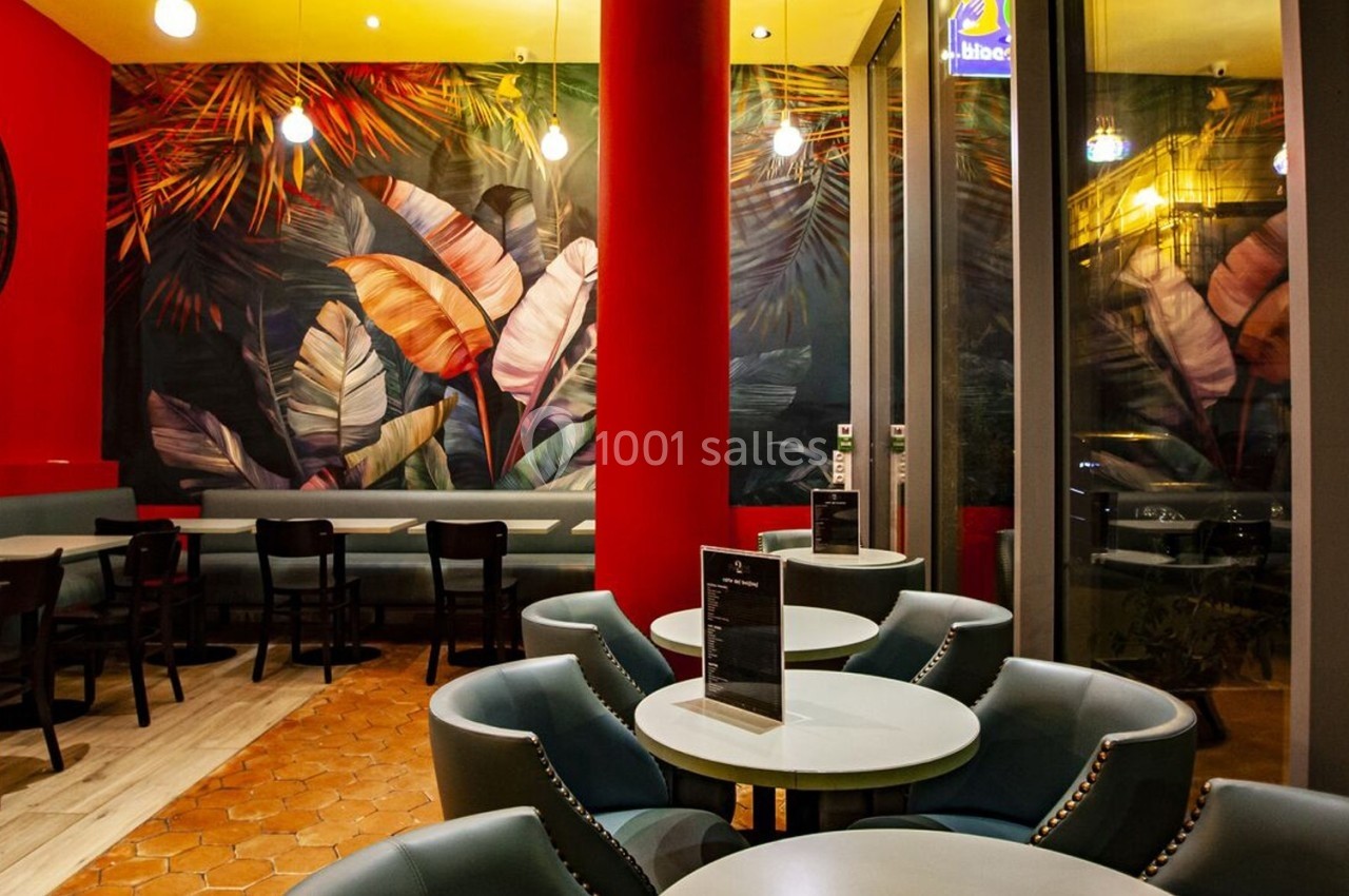 Salle de restaurant colorée avec murs décorés de motifs tropicaux, mobilier moderne et éclairage chaleureux.