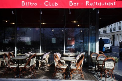 Façade d'un café-restaurant avec terrasse extérieure, tables et chaises sous un auvent rouge marqué ’Les 2 Pianos’.