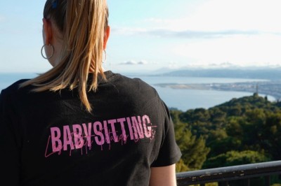 Une femme surveille deux jeunes enfants jouant avec des jouets dans un bac à sable en plein air.