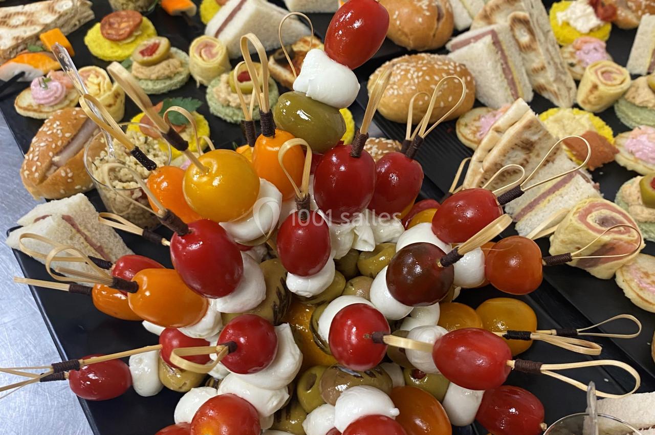 Plateau de buffet avec brochettes de tomates cerises et mozzarella au premier plan, entouré de divers amuse-bouches.