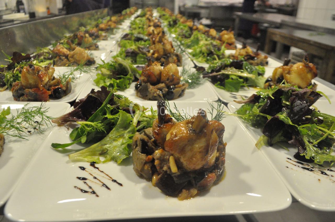 Assiettes dressées avec des légumes, salades et morceaux de viande, alignées dans une cuisine professionnelle.