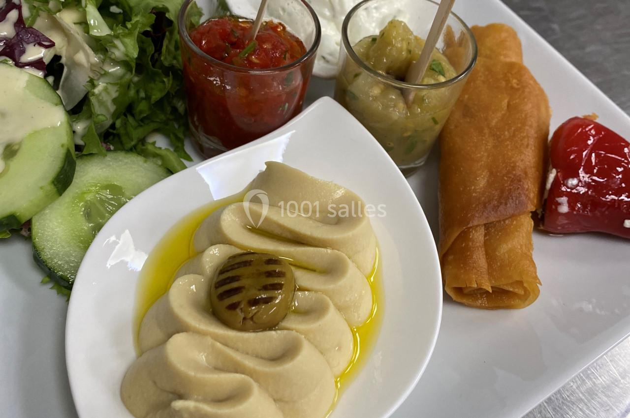 Assiette composée de houmous, sauces variées, salade verte, rouleaux croustillants et légumes grillés.
