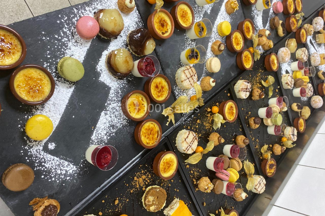 Plateaux garnis de desserts variés, incluant macarons, crèmes brûlées, verrines et pâtisseries, présentés sur ardoises.