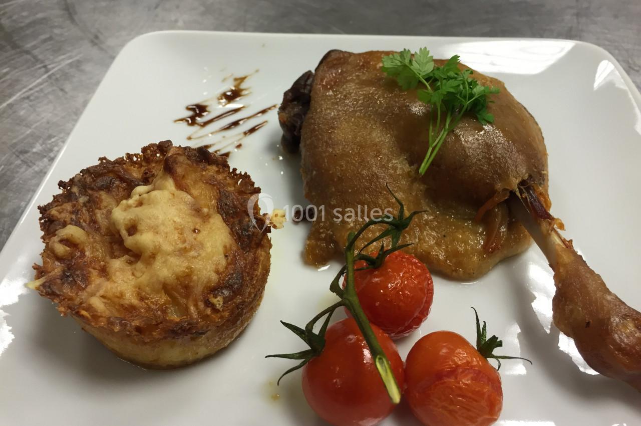 Cuisse de canard confite avec gratin de pommes de terre et tomates cerises rôties, servie sur une assiette blanche.