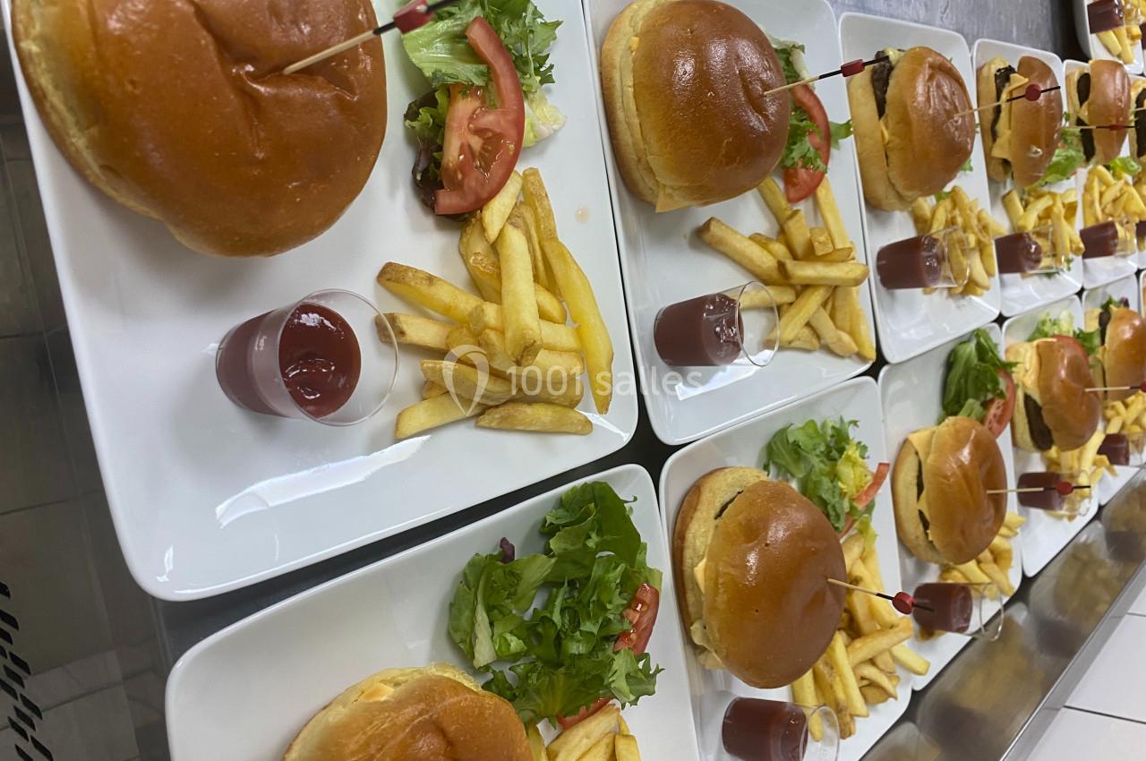 Assiettes contenant des burgers, frites, salade et une verrine de sauce, alignées sur un plan de travail.