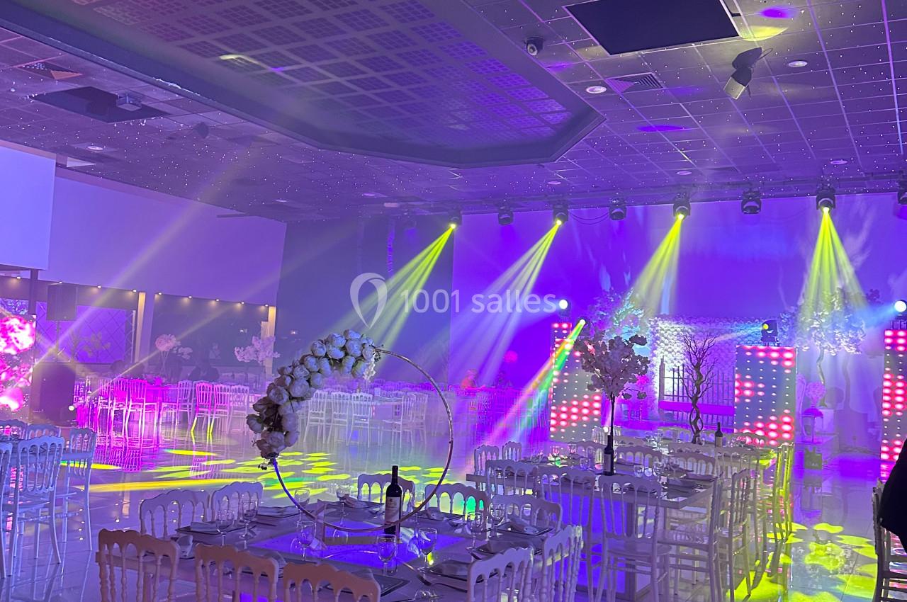 Salle de réception décorée avec des tables et des chaises, éclairée par des lumières colorées et des projecteurs.