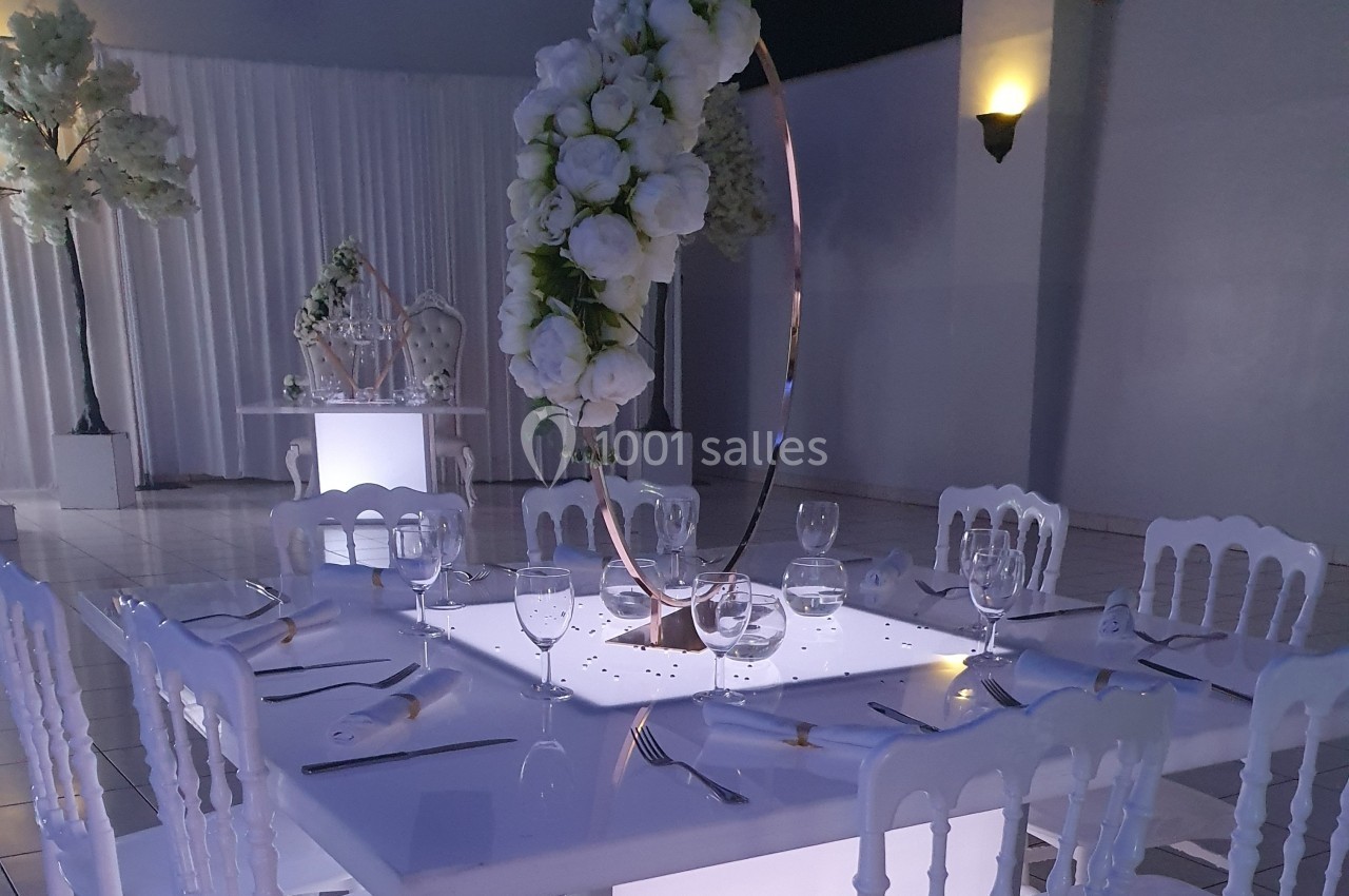 Table élégamment dressée avec des assiettes, verres et couverts, décorée de fleurs blanches sur un anneau doré.