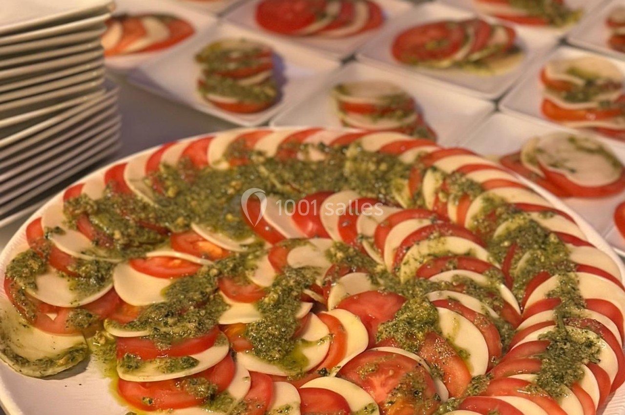 Assiette de salade caprese avec des tranches de tomate, mozzarella et pesto, entourée d'autres assiettes similaires.