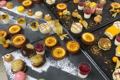 Plateaux garnis de desserts variés, incluant macarons, crèmes brûlées, verrines et pâtisseries, disposés sur un plan de…