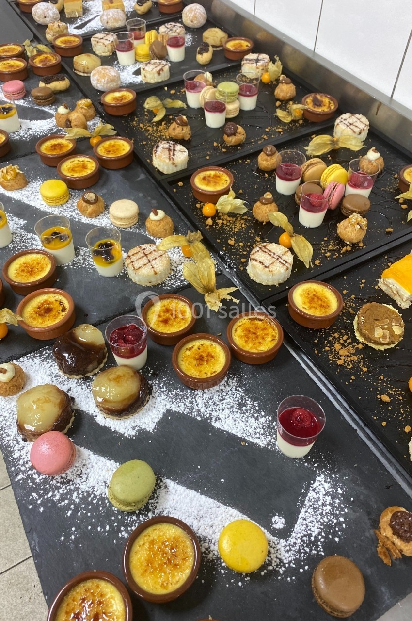 Plateaux garnis de desserts variés, incluant macarons, crèmes brûlées, verrines et pâtisseries, disposés sur un plan de…