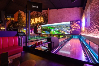 Salle de restaurant moderne avec bar illuminé, tables en bois, chaises colorées et décoration murale végétale.