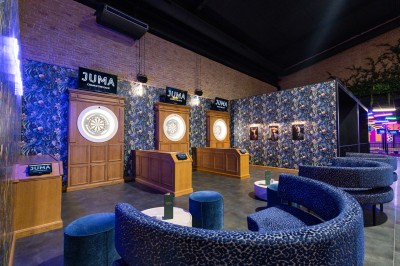 Salle de restaurant moderne avec bar illuminé, tables en bois, chaises colorées et décoration murale végétale.