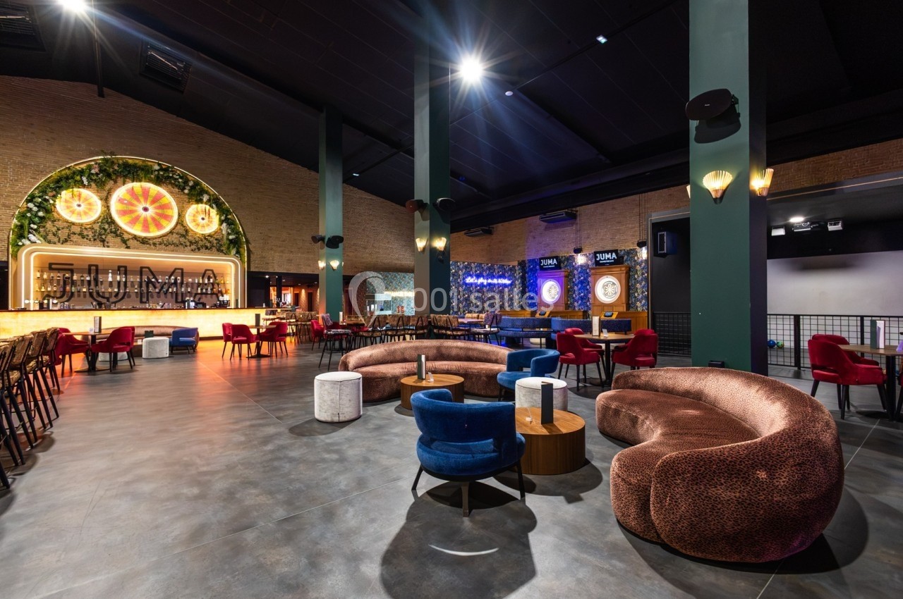Intérieur d'un bar spacieux avec des fauteuils colorés, un éclairage chaleureux et un décor mural végétal.