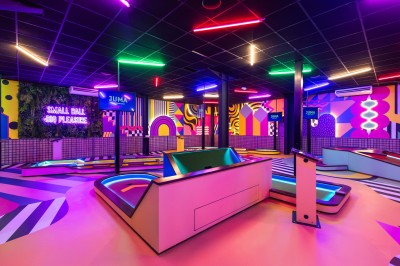 Salle de restaurant moderne avec bar illuminé, tables en bois, chaises colorées et décoration murale végétale.